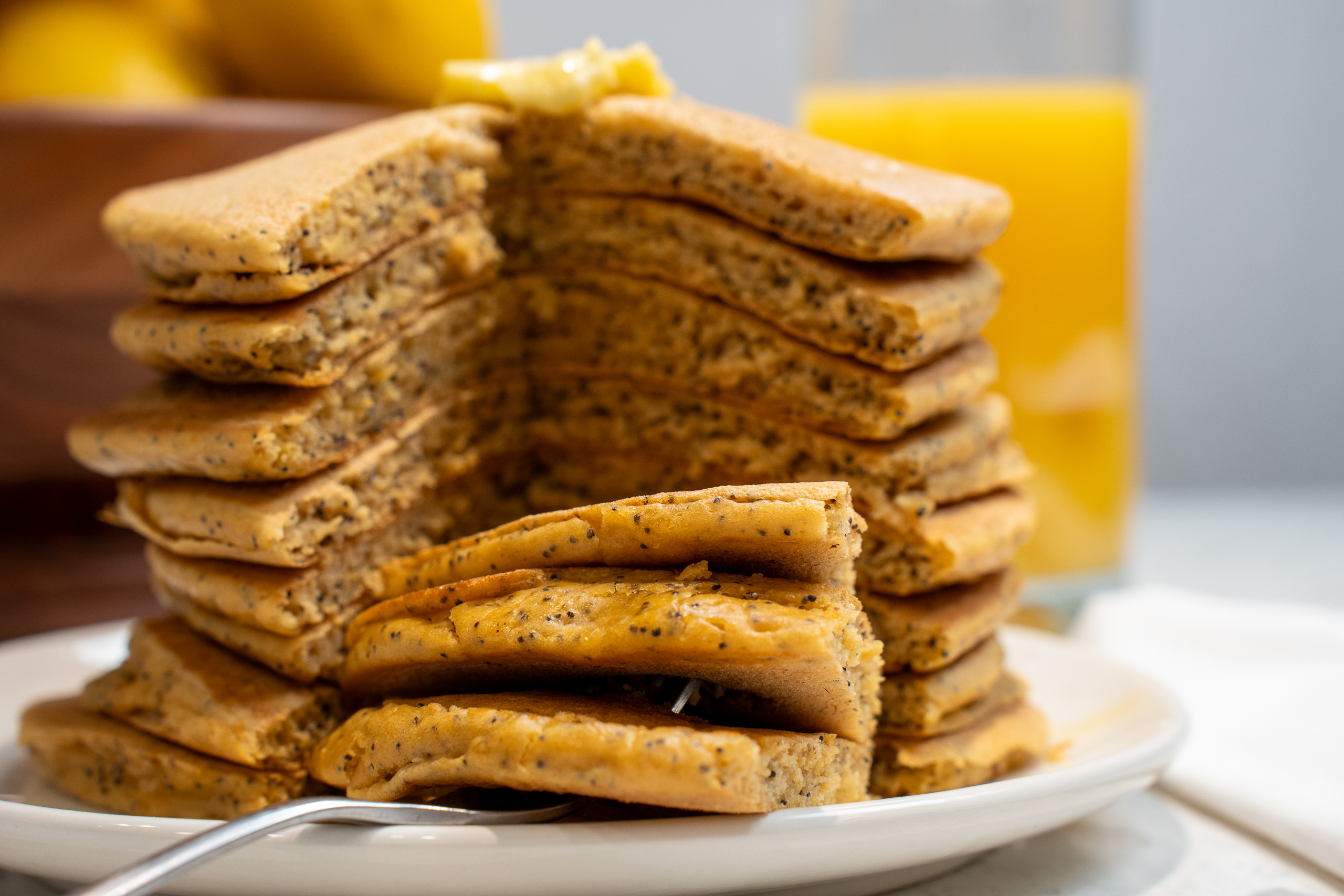 Lemon Poppy Seed Pancakes stack on a plate with lemon slices and honey drizzle, served on a white plate.